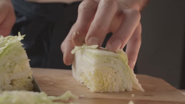 Front View of Young Man Chef Cut Thin Slices of a Piece Green Cabbage with Knife