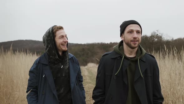 Two Young Guys Walking On The Road In Nature. They Joke And Laugh.