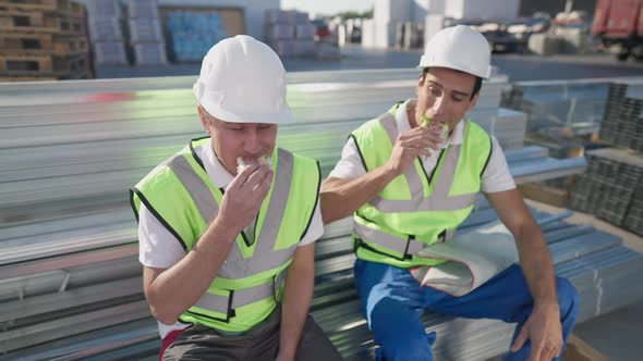 Portrait of Caucasian Man in Hard Hat Chewing Sandwich Thanking Middle Eastern Coworker for Lunch