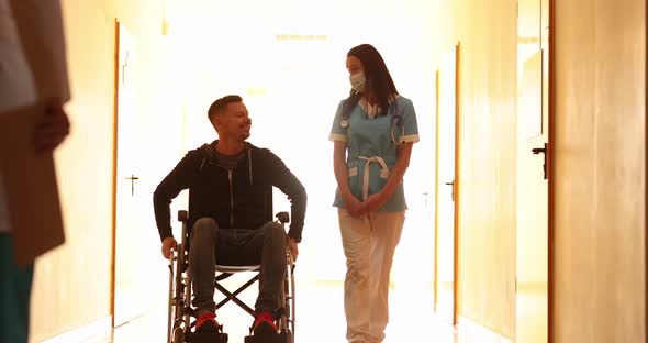 Nurse Walking with Patient in Wheelchair Down Hallway and Greeting Doctor  Movie Slow Motion