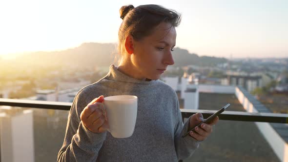 Woman Starts Her Day with a Cup of Tea or Coffee and Checking Emails in Her Smartphone on the