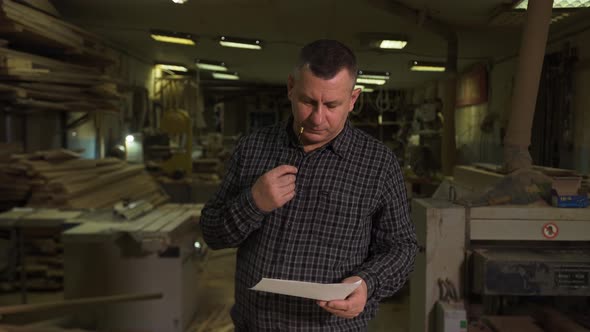 Engineer in Shirt Stands Against Background of Production with Sketch on Paper