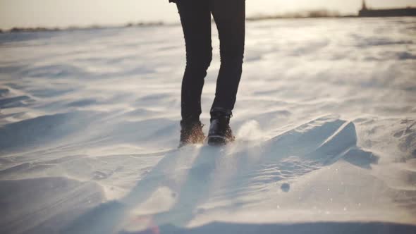Closeup of Woman's Feet Walking on the Snow Desert at Sunset 