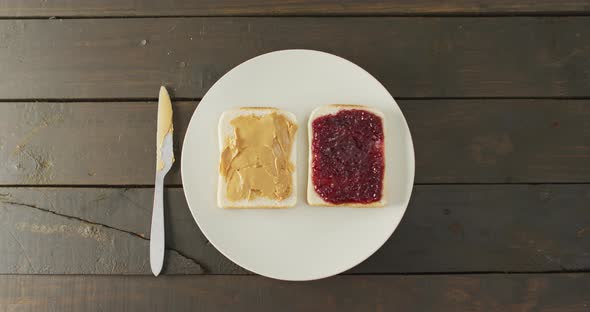 Close up view of peanut butter and jelly sandwich in a plate with butter knife on wooden surface