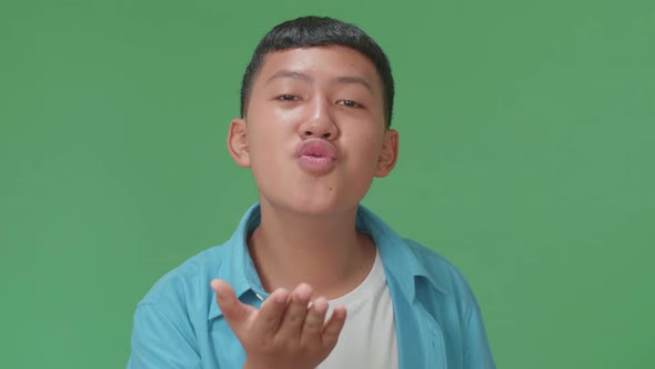 Portrait Of A Smiling Young Asian Boy Blowing Kisses To A Camera In The Green Screen Studio