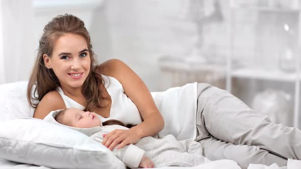 Smiling Caring Mother Posing Lulling Sleepy Cute Baby Hugging and Touching Feeling Love Medium Shot