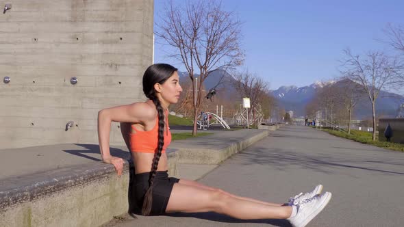 Young Hispanic woman doing triceps dip exercise on cement stair, Side View