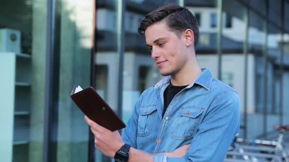 Male Student Reading Notepad Outdoors At College