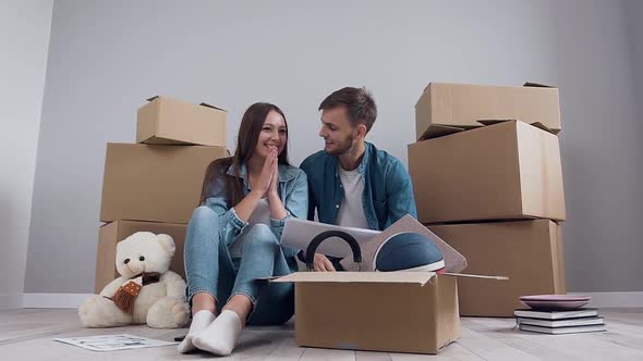 Appealing Joyful Pair in Love Sitting on the Floor Among Many Boxes in the New Apartment