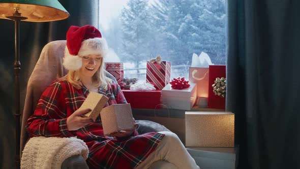 Blonde Woman in Funny Red Santa Claus Hat Sitting in Cozy Living Room Fireplace