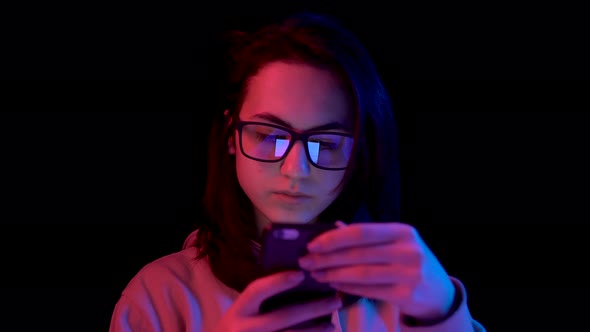 Young Woman with a Smartphone. Woman Use the Phone. Blue and Red Light Falls on a Woman on a Black