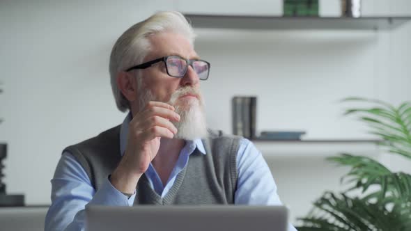 Thoughtfulan Elderly Business Man with a Gray Beard Thinking of Problem Solution Working on Laptop.