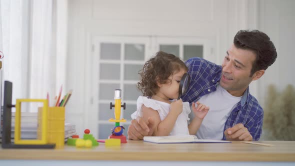 Little girl doing science experiments in the laboratory with father looks through magnifying glass