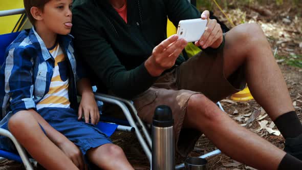 Father and son taking a selfie on mobile phone outside tent