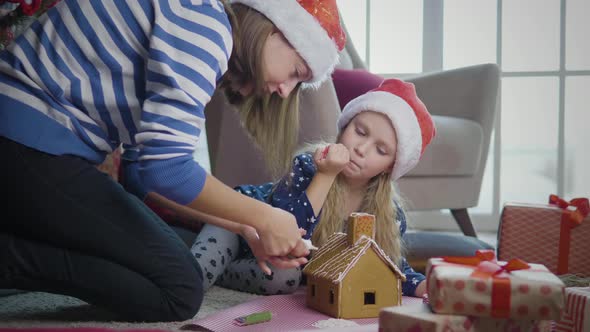 Mother with daughter decorates gingerbread house