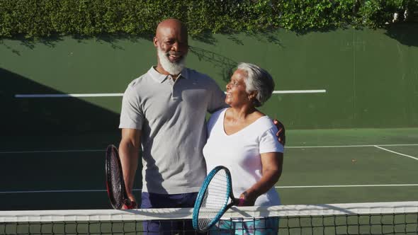 Portrait of african american senior couple holding rackets standing on the tennis court