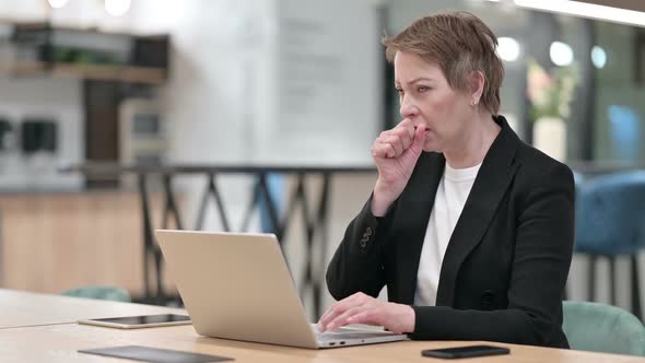 Sick Old Businesswoman with Laptop Coughing in Office