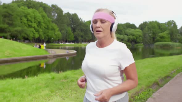 Tired Mature Woman in Sportswear and Headphones Jogging in Park