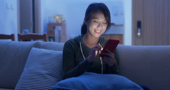 Woman use of smart phone sit on sofa at home in evening