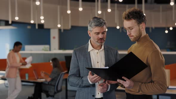 Two Male Colleagues Standing Together at Business Center and Discussing Common Project