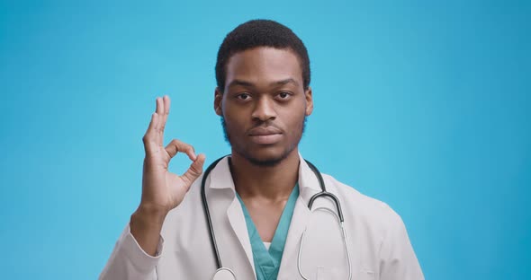 Confident Professional African American Medical Doctor Gesturing OK Sign, Blue Background