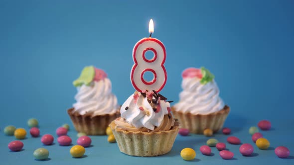 Cake Birthday Cupcake with a Burning Candle Number Eight 8 on a Blue Background