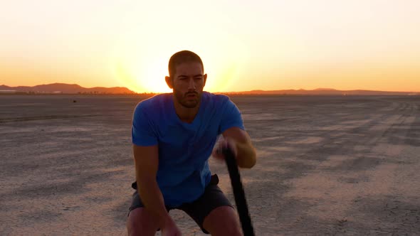 Athletic man working out with battle ropes on a dry lake at sunset