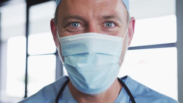 Portrait of caucasian male doctor wearing face mask looking at camera