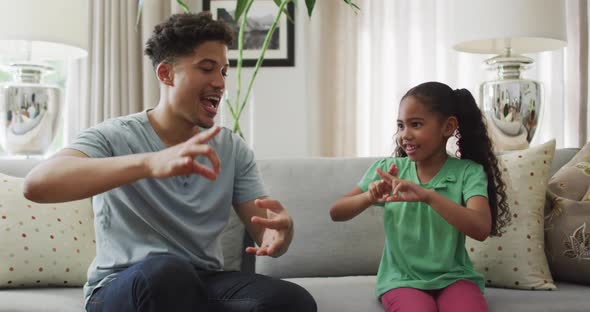 Happy biracial father and daughter sitting on sofa using sign language