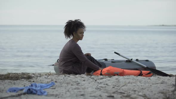 Frozen Teenage Girl Sitting Near Boat on Seashore, Shipwreck Refugee Survivor