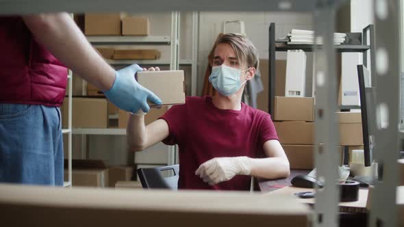 Man Employee of Warehouse Wearing Medical Mask and Protective Gloves Receiving Delivery Box and