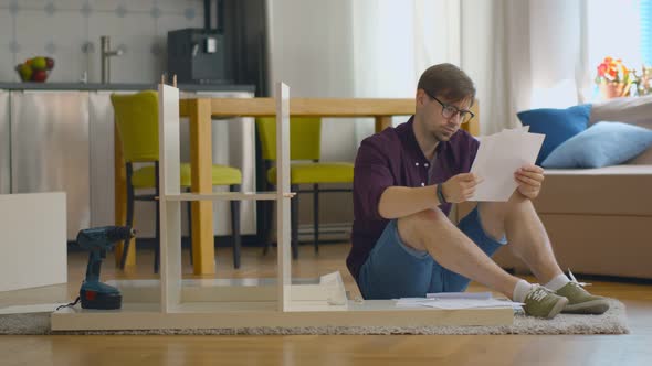 Concentrated Young Man Reading Instructions To Assemble Furniture in Kitchen at Home