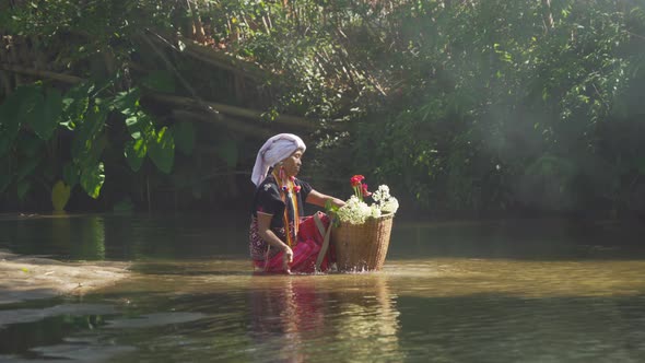 A karen tribe old woman with traditional dress carrying flowers basket sitting in stream lake