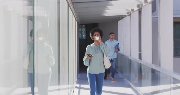 Video of african american businesswoman walking with smartphone and coffee in office