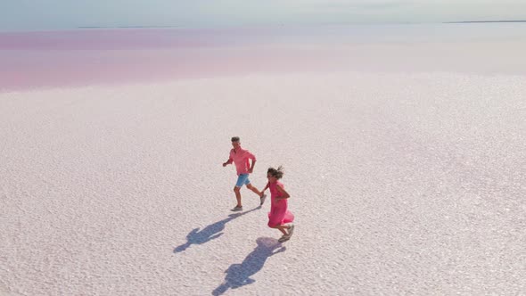 Aerial Drone Footage of Happy Young Couple in Pink Wear Having Fun and Joyfully Running on White