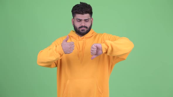 Confused Young Overweight Bearded Indian Man Choosing Between Thumbs Up and Thumbs Down