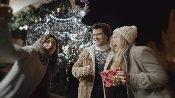 Three Friends Dancing with Gifts in Hands at Xmas Night at Old Town Square