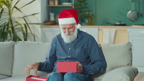 Happy Elderly Man Smiling Enthusiastically Opening a Box With Christmas Present