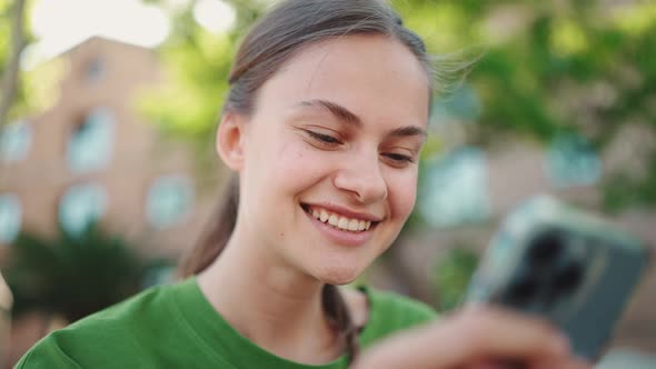 Smiling blonde woman wearing green t-shirt texting by phone on the bench