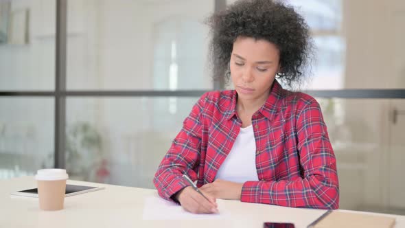 African Woman Writing on Paper in Office