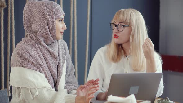 Two Female Friends Are Chatting in Cafe and Watching on Display of Laptop