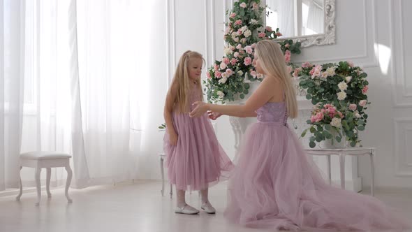 Little cheerful girl in purple puffy dress having fun next to her mother in white room
