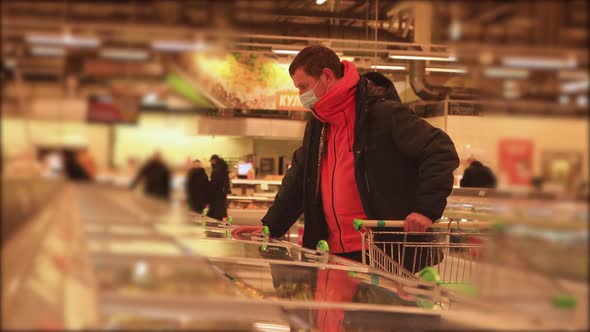 A Man in a Supermarket Picks Up Mormite Products with a Mask on His Face