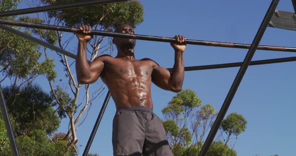 Fit, shirtless african american man exercising outside, doing chin-upso n a climbing frame