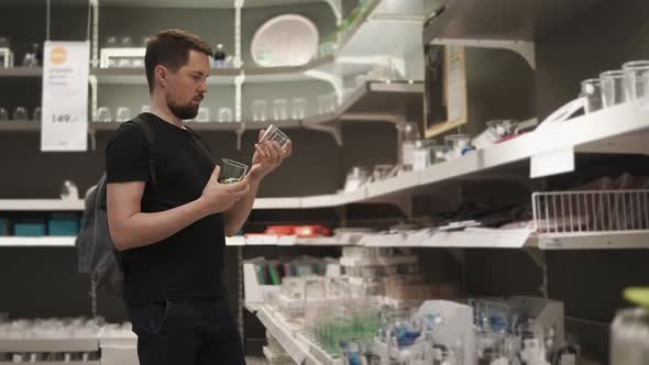 Man is Standing in a Sale Area of Tableware Store and Holding Two Glasses