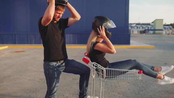 Guy Rolls Attractive Young Woman in the Trolley in Motorcycle Helmets at Sunset