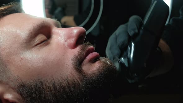 Barber Shaves the Client's Beard on a Chair. Beard Haircut. Barber To Shave a Beard with an Electric