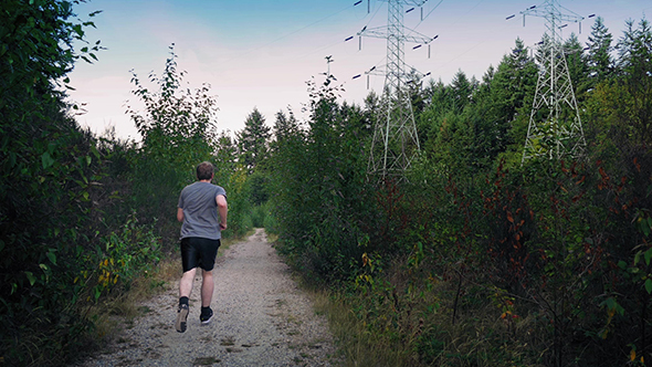 Man Runs On Gravel Path In Forest Near Power Lines