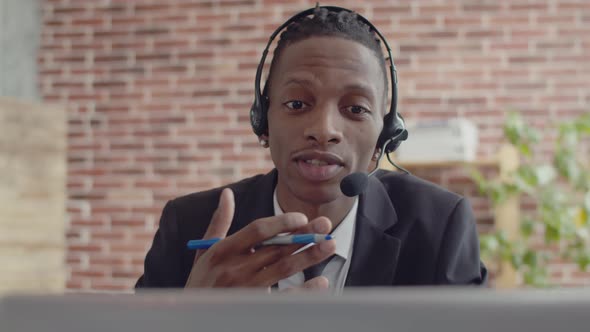 Black man operator in headset and office suit speaks via video link on a laptop