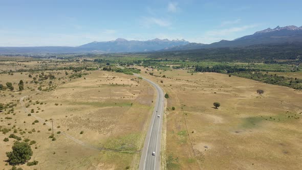 Aerial dolly in following a lonely countryside road with mountains in background at daytime